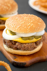 Homemade Mississippi Slug Burgers with onion rings on a rustic wooden board, side view. Close-up.