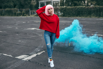 Fototapeta premium Stylish Asian woman with blue smoke bomb on background