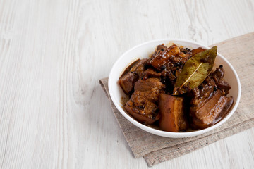 Homemade Filipino Adobo Pork in a bowl on a white wooden background, side view. Copy space.