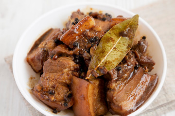 Homemade Filipino Adobo Pork in a bowl on a white wooden background, side view. Close-up.