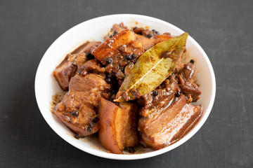 Homemade Filipino Adobo Pork in a white bowl on a black surface, side view. Close-up.