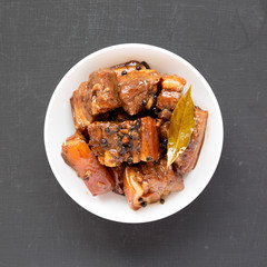 Homemade Filipino Adobo Pork in a white bowl on a black surface, top view. Flat lay, overhead, from above. Close-up.
