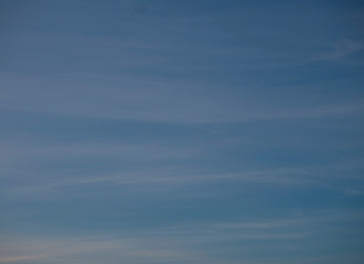Blue sky with thin white stripes of clouds background. Beautiful panoramic sky with upcoming twilight.
