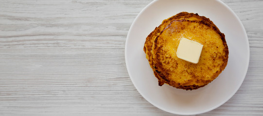 Homemade corn meal Johnny cakes  on a white plate on a white wooden surface, top view. Flat lay, from above, overhead. Space for text.