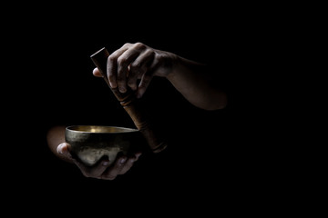 Hands  playing an old tibetan singing bowl. Black background. Music therapy.