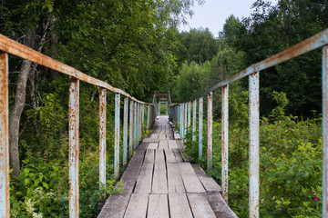 old suspension bridge over a small river in the forest in summer, bridge elements