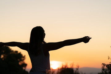 Fototapeta na wymiar silhouette of womasilhouette of young woman with open arms raised in a sunsetn relaxing her arms at sunset