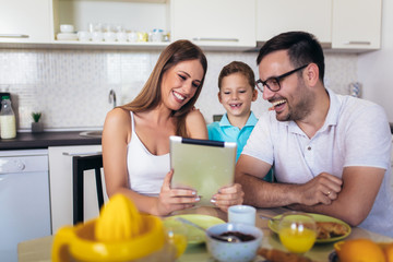 Obraz na płótnie Canvas Family eating breakfast at kitchen table using digital tablet