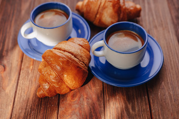 two cups of coffee and croissants on a wooden background, good light, morning atmosphere