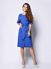 Slender curly female model in a blue urban dress in full growth. Lovely girl in romantic clothes goes on a date, to the office, to a meeting. Urban fashion