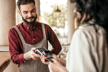 Hipster waiter giving customer machine for card payment at coffee shop