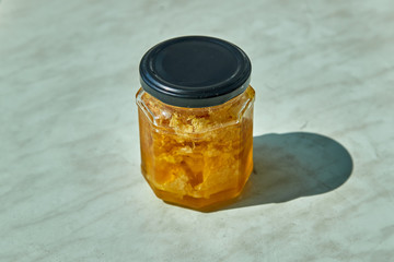 Raw honeycomb with liquid honey in glass jar on the table.