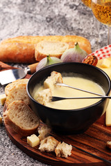 Gourmet Swiss fondue dinner on a winter evening with assorted cheeses on a board alongside a heated pot of cheese fondue with two forks dipping