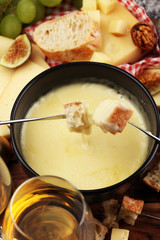 Gourmet Swiss fondue dinner on a winter evening with assorted cheeses on a board alongside a heated pot of cheese fondue with two forks dipping