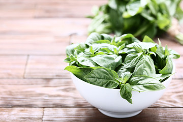 Green basil leafs in bowl on brown wooden table