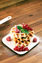 Traditional belgian waffles with fresh mint, sugar and raspberries on table