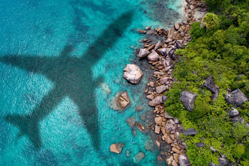 Concept of airplane travel to exotic destination with shadow of commercial airplane flying above beautiful tropical beach. Beach holidays and travel.