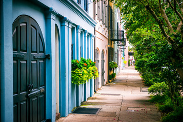Fototapeta premium Widok pusty chodnik na bujną letnią zieleń otaczającą kolorową gruzińską architekturę kolonialnej Rainbow Row w historycznej dzielnicy Battery w Charleston w Południowej Karolinie, USA