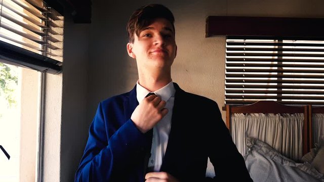 Confident young teenager male preparing tie in mirror for formal prom event.