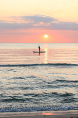 Fototapeta premium Woman's silhouette on a paddle board (SUP) at a beautiful pink pastel gradient sunset.