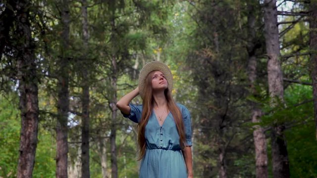 Young beautiful woman walking through a pathway in a pine forest. Fashion woman in dress and hat, walks through the forest, looks around, enjoys the nature. Concept: recreation, beautiful view, travel