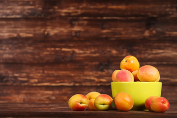 Sweet apricots in bowl on brown wooden table