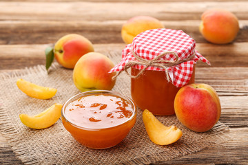 Apricot jam in bowl and jar on brown wooden table