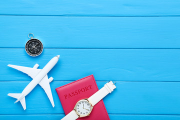 Airplane model with passport, wrist watch and compass on blue wooden table
