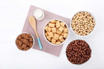 Various corn flakes with bottle of milk and spoon on white wooden table