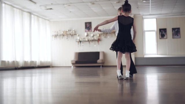 Wide shot of two cute children dancing in an empty hall during a dance lesson