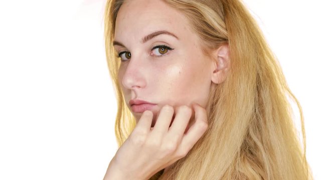 In slow motion, against a white backdrop, a blonde woman poses confidently
