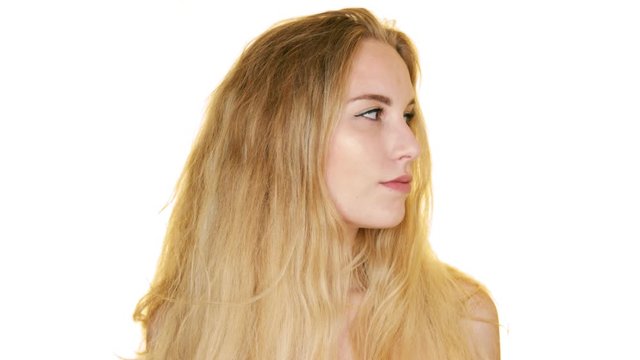 Pretty blonde girl looks from side to side, posing against a white backdrop, touching her face with her hands