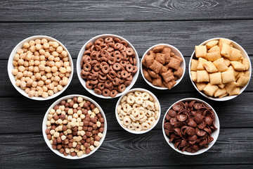 Various corn flakes in bowls on black wooden table