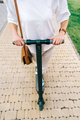 Unrecognizable woman riding an electric scooter in summer park.