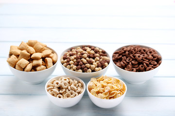Various corn flakes in bowls on white wooden table