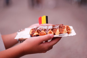 hand of a girl holding a chocolate waffle with brussels flag in a street of Ghent