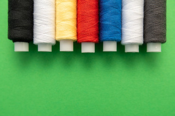 Set of sewing threads beautiful color (blue,yellow, green, white, black) on green background with space for text