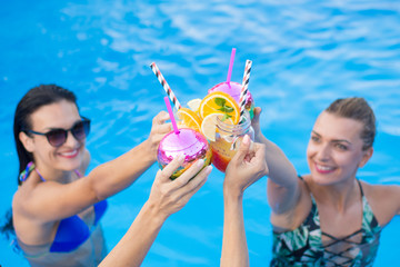 Group of women hanging out by the swimming pool and having cocktails on summer day.