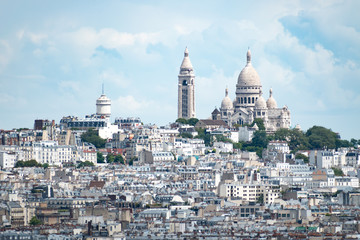 Fototapeta na wymiar View of the Sacré-Cœur at the top of Montmartre Hill in Paris, France, on a bright cloudy day, with buildings in the foreground covering the steep hillside.