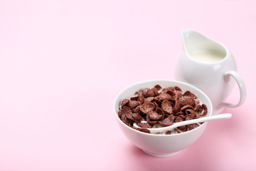 Chocolate corn flakes in bowl with milk and jar on pink background