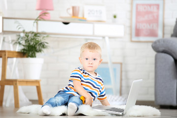 Naklejka premium Little boy with laptop computer sitting on white carpet at home