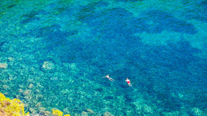 Fototapeta premium Two divers dive on the surface of the sea in a beautiful bay on a sunny summer day. Water activities, vacation at sea, happy holidays in the Mediterranean.