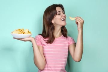 Young woman with potato chips in plate on mint background