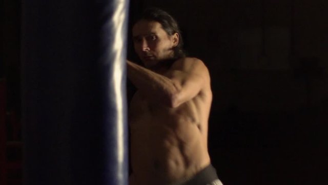 a man with long hair and a strong torso is training, taekwondo, beating his hands and feet on a boxing bag