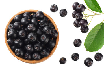 Chokeberry in wooden bowl with green leaves isolated on white background. Black aronia. Top view.