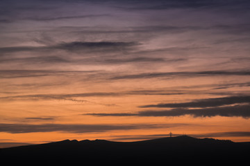 Silhouettes of mountains against a bright sunset. The sun sets over the hills. Cross on top.