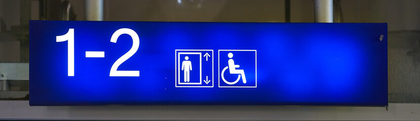 Neon sign with wheelchair symbol in the direction of the elevator at a train station.