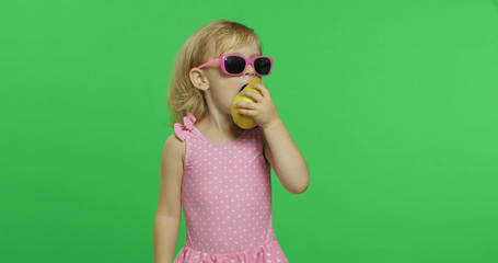 Child in pink swimsuit and sunglasses eats a green pear. Chroma Key