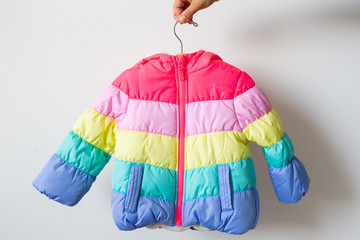 Woman holding rainbow toddlers puffer jacket on hanger, white background