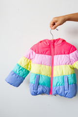 Woman holding rainbow toddlers puffer jacket on hanger, white background